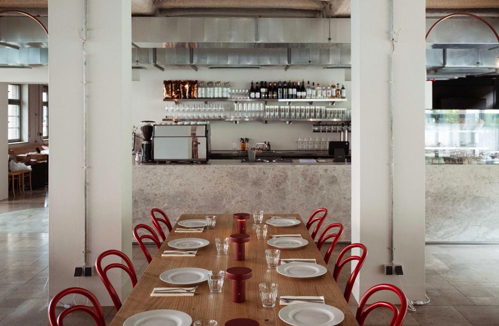 Tafel gedeckt mit Besteck und roten Stühlen, Bar im Hintergrund.